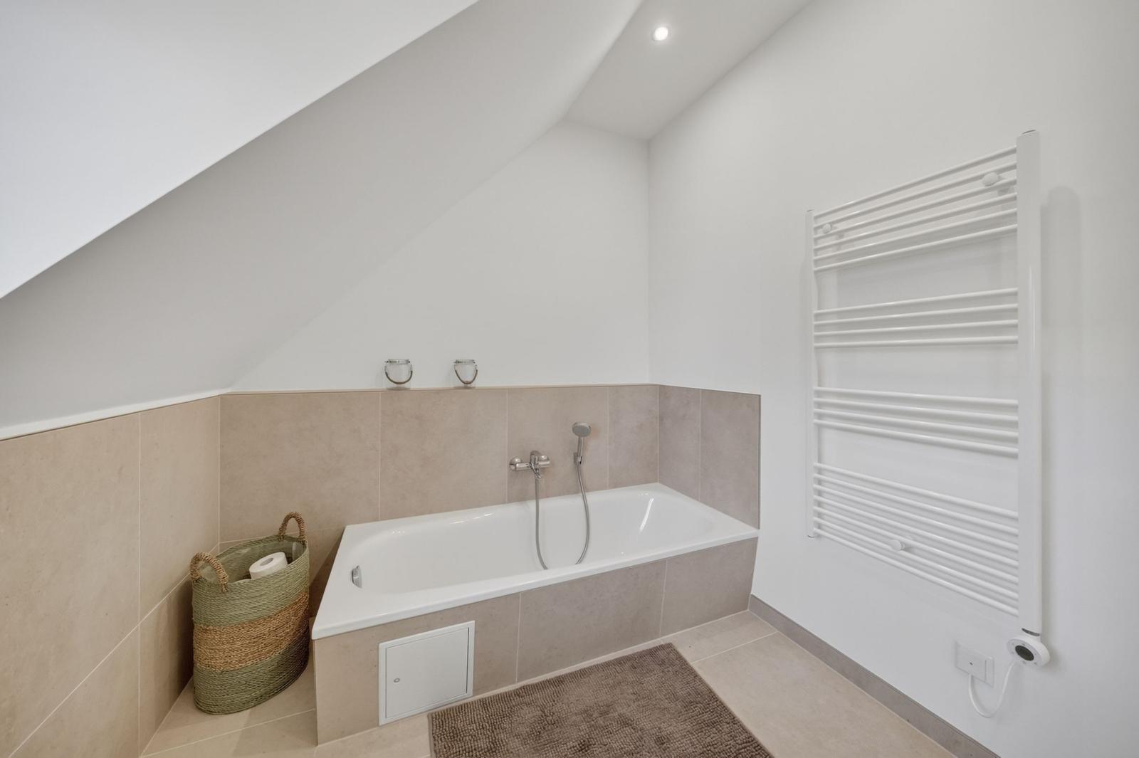 Badezimmer mit Badewanne, Heizkörper und geflochtenem Korb.