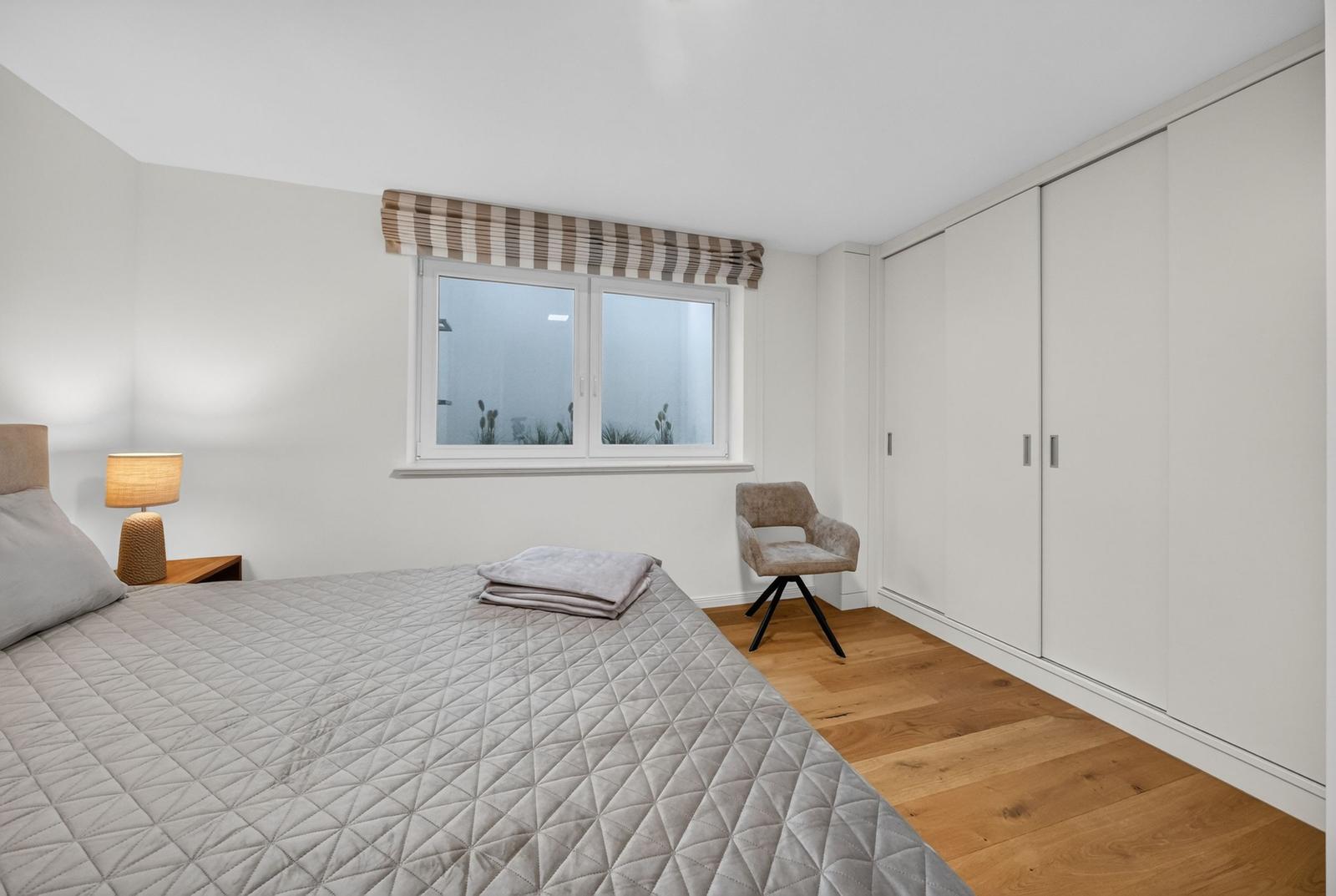 Schlafzimmer mit Bett, Kleiderschrank und Fenster mit Markisen.