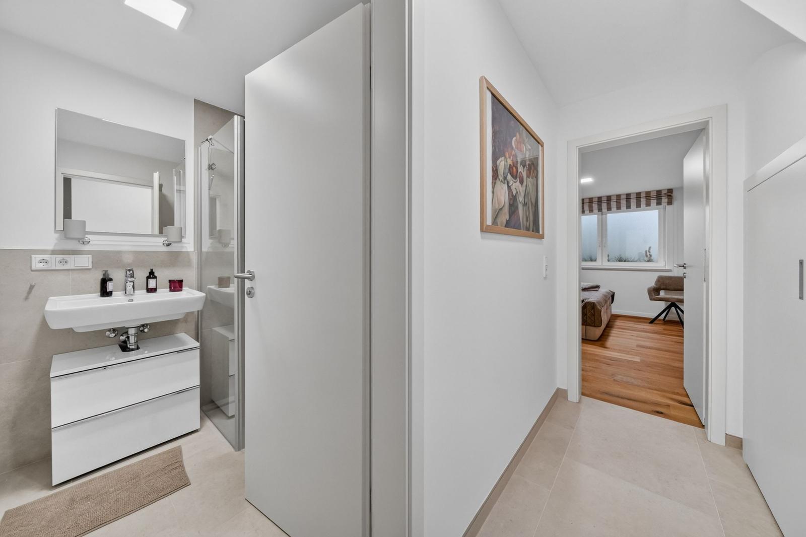 Flur mit Bad und Schlafzimmer. Bad mit Waschbecken und Dusche. Schlafzimmer mit Holzboden.