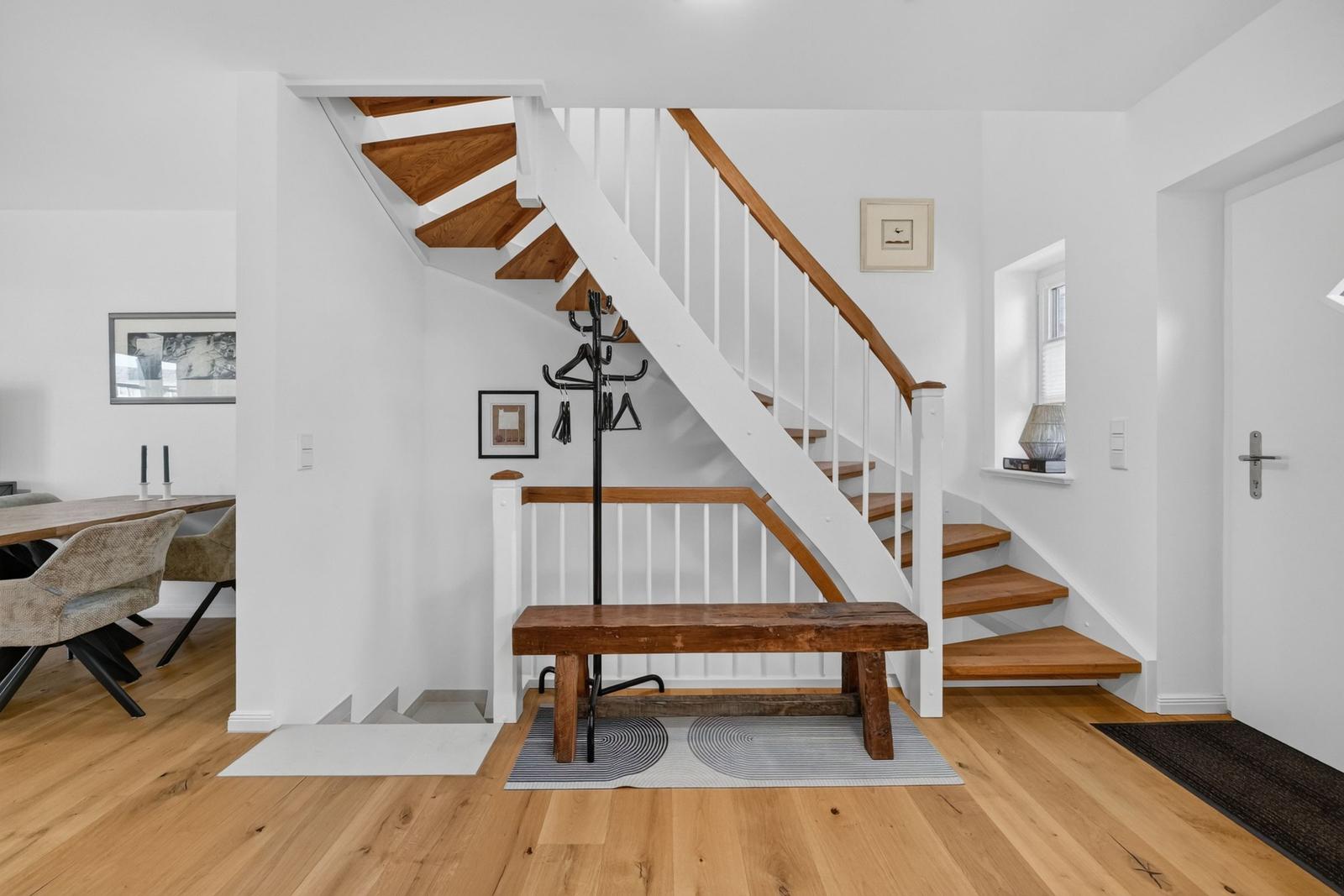 Haus mit Holztreppe, Bank und Garderobe im Eingangsbereich. Holzfußboden und weiße Wände.