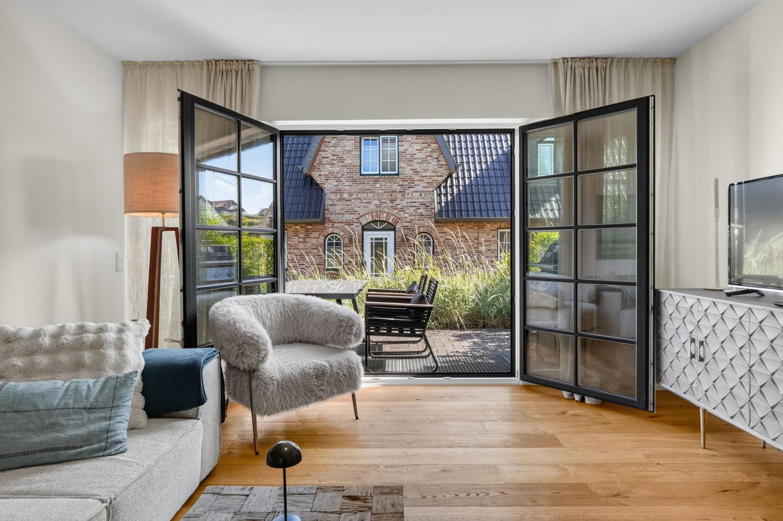 Wohnzimmer mit Blick auf Terrasse und Haus. Möbel und Holzboden sichtbar.