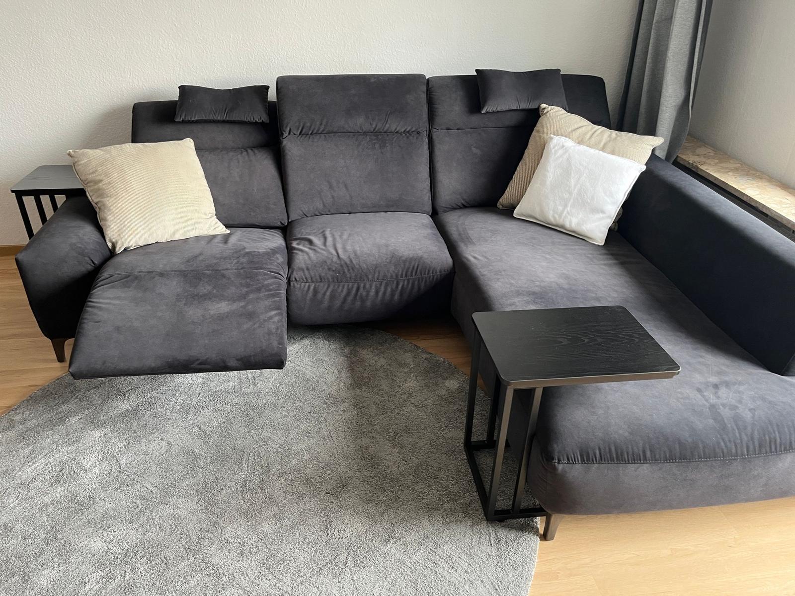 Ein grauer Ecksofa mit Kissen und zwei kleinen Tischen auf Teppich und Holzfußboden.