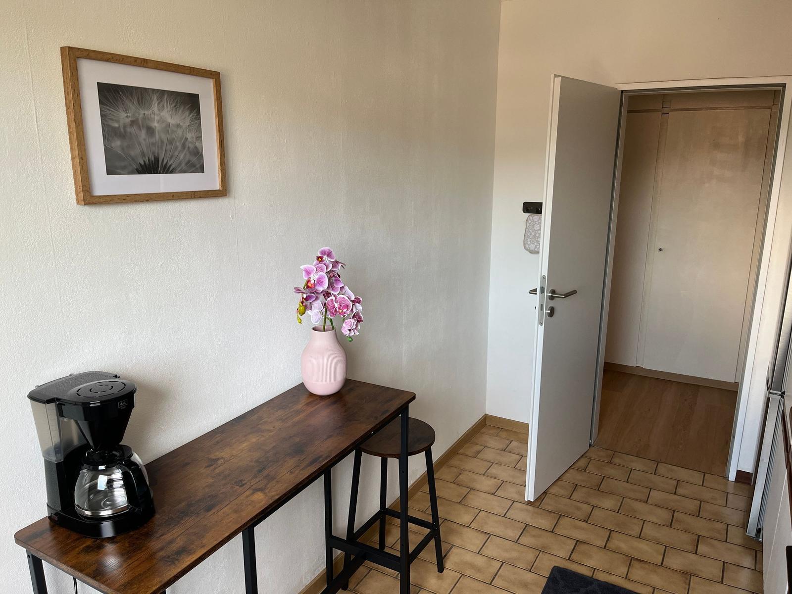 Tisch mit Kaffeemaschine und Orchidee, Tür führt in den Flur.