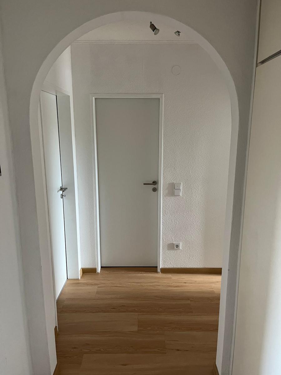 Höhenbogen führt in einen Flur mit Holzboden und weißen Türen.