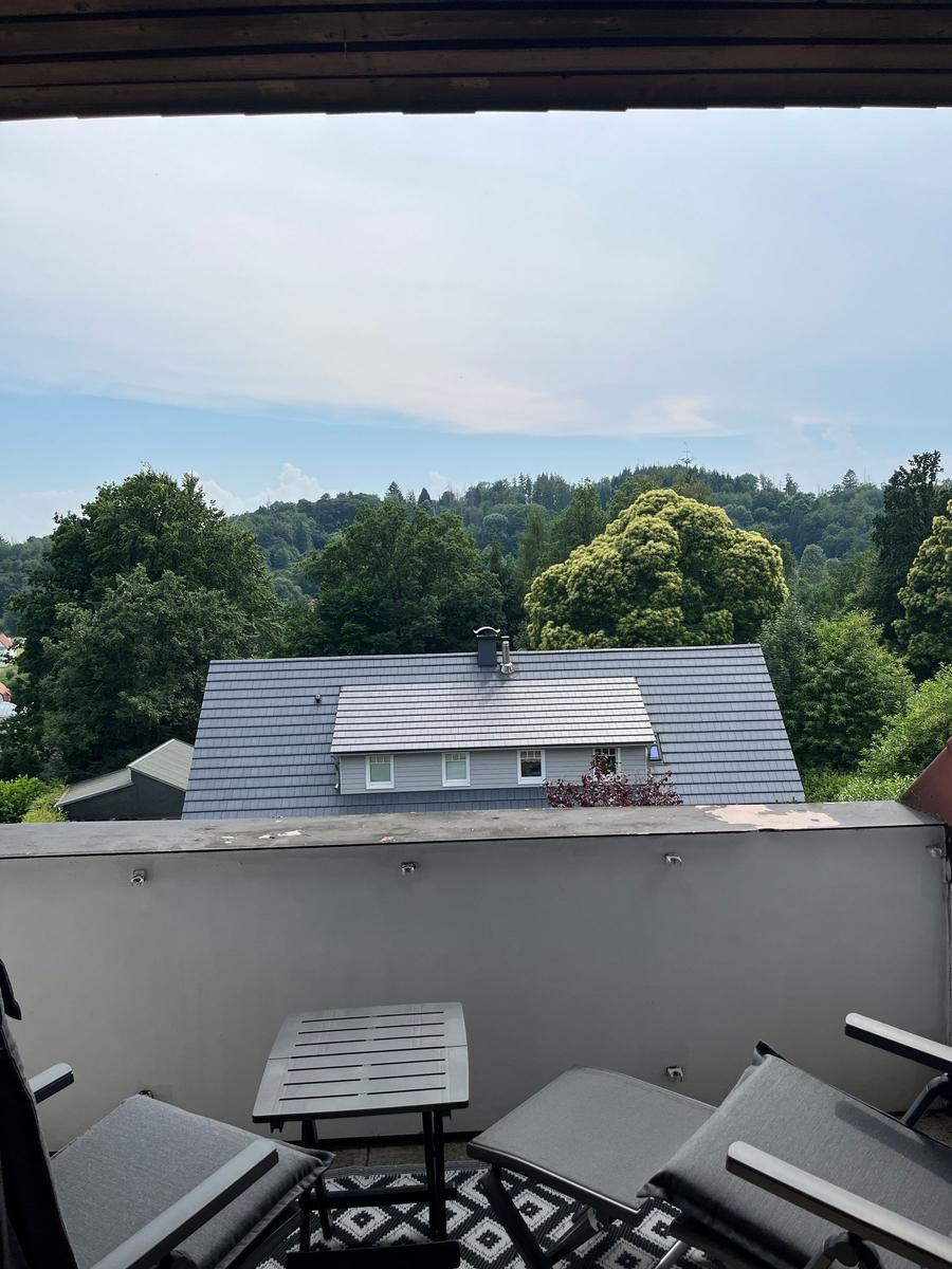 Terrasse mit Sitzgelegenheiten und Blick auf ein Haus und Wald.