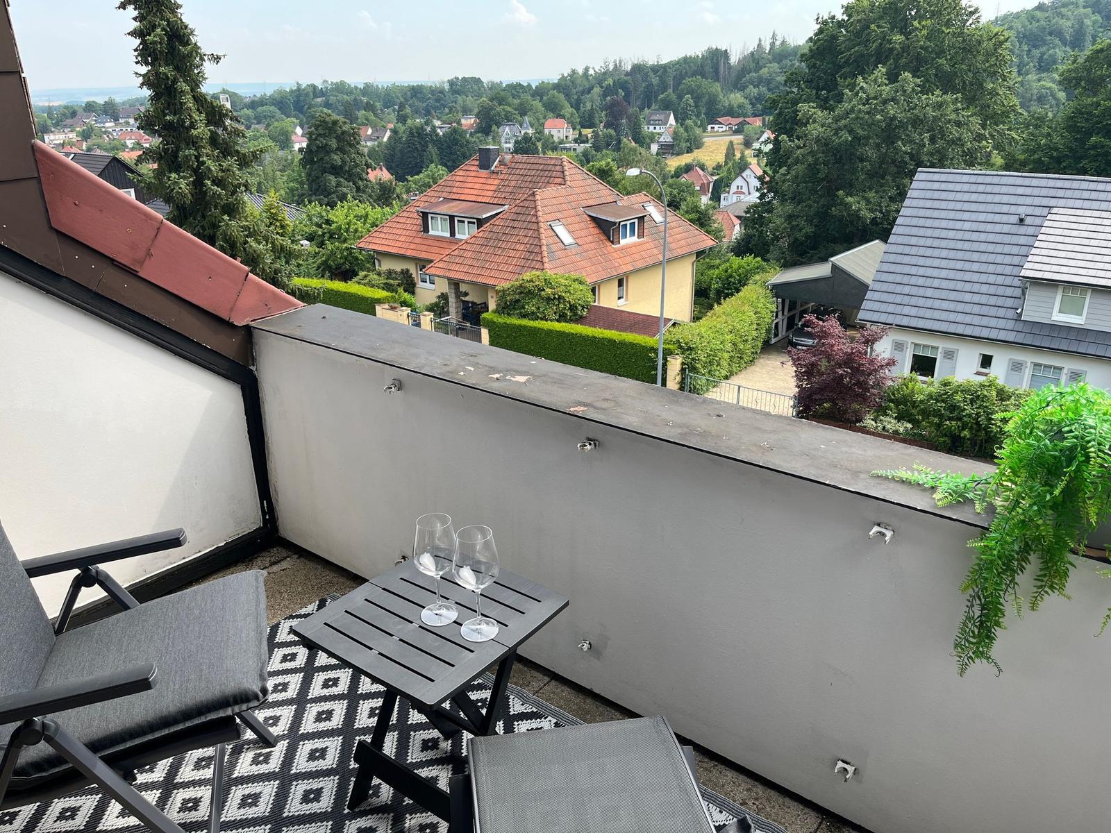 Terrasse mit Tisch, zwei Stühlen und Blick auf Wohnhäuser und Grünflächen.