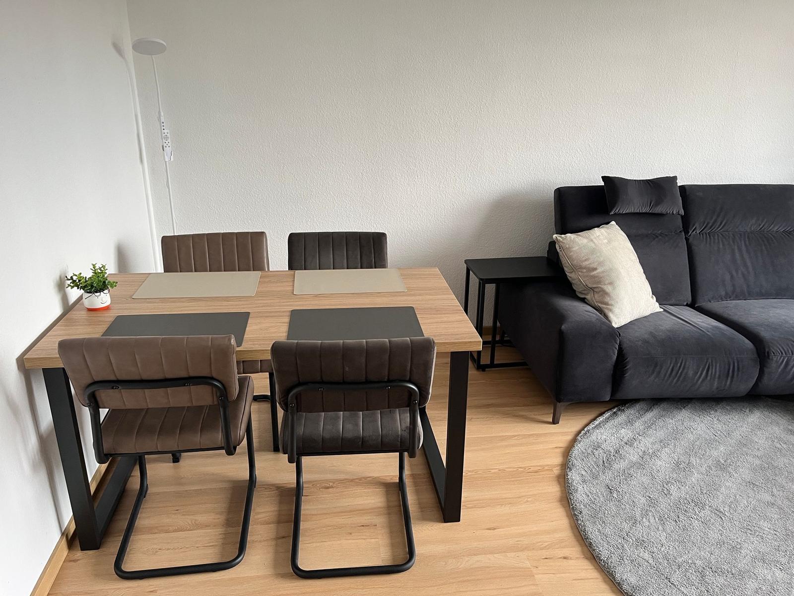 Essbereich mit Tisch und vier Stühlen neben einem dunklen Sofa.