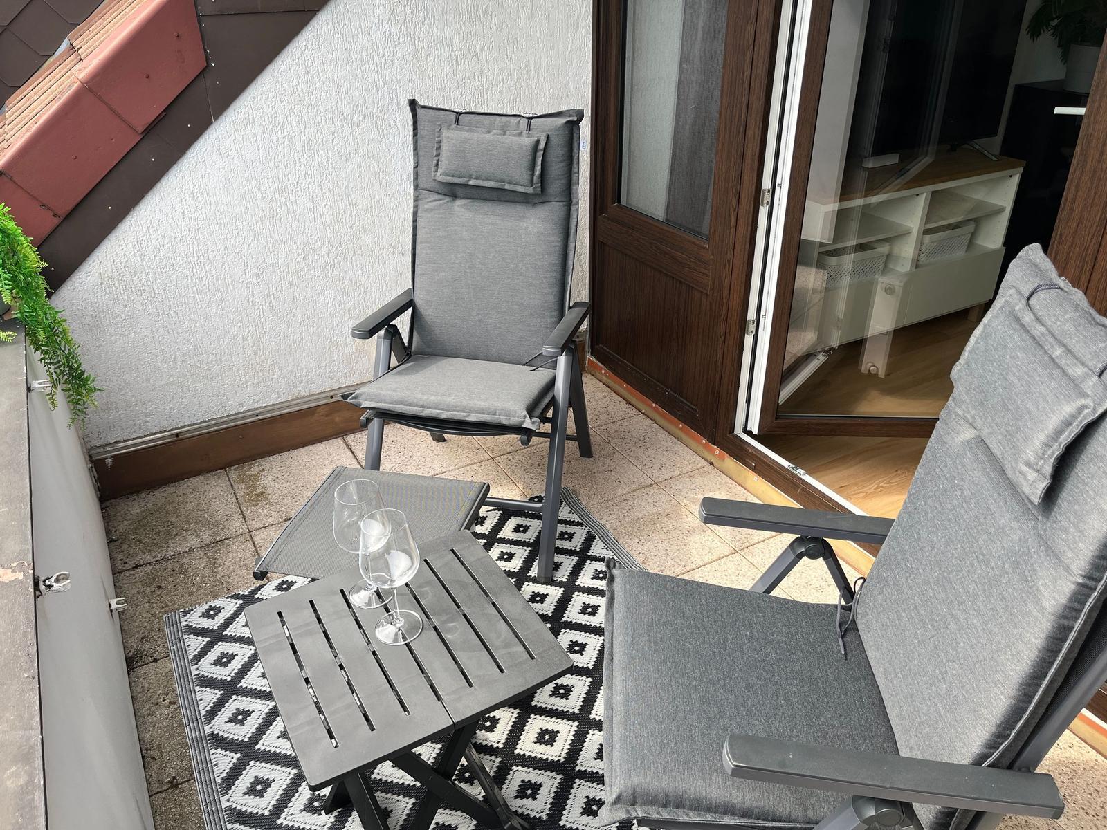 Terrasse mit zwei grauen Sesseln, Tisch und Teppich. Durchgang ins Haus.