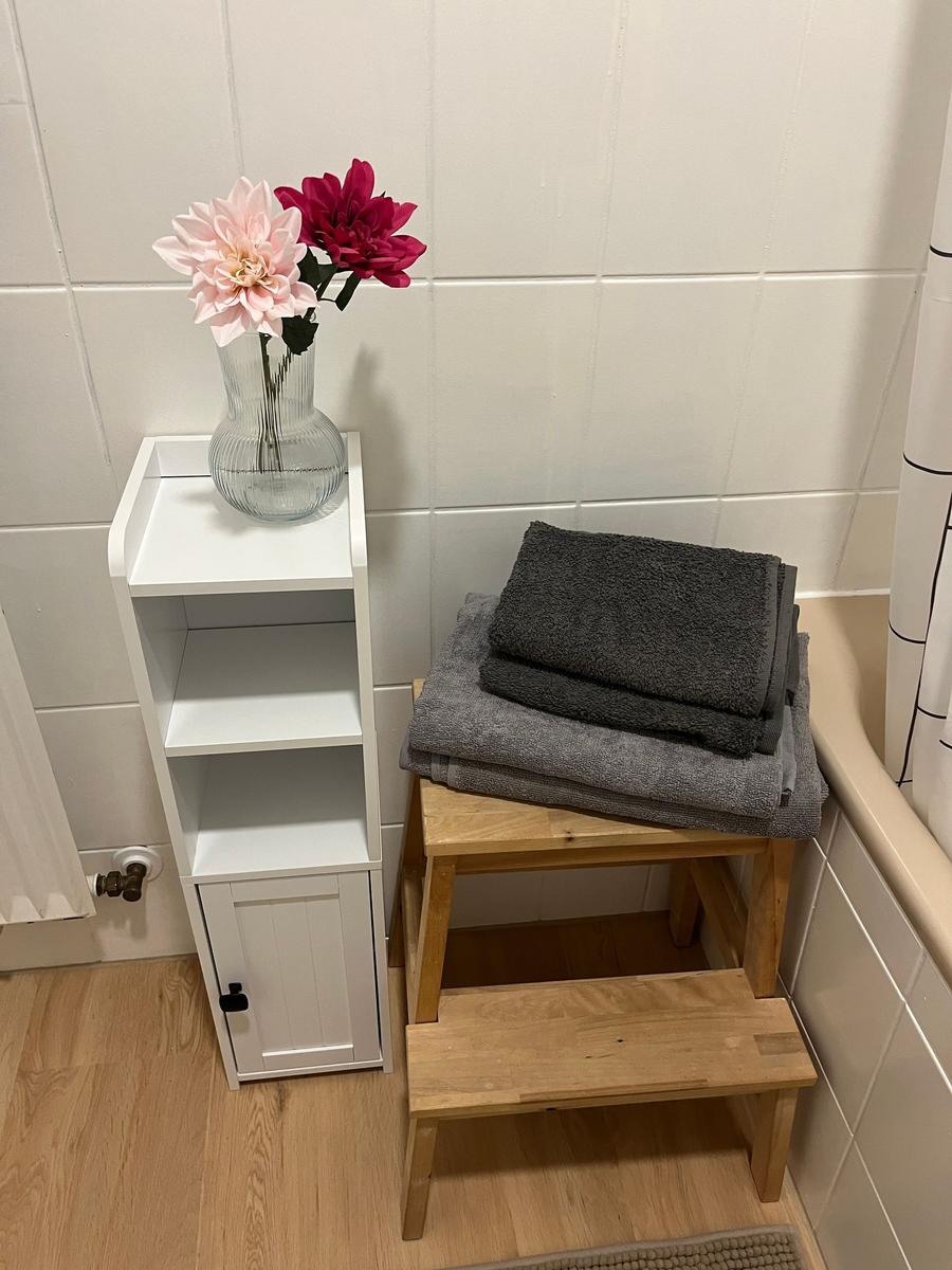 Bad mit weißen Fliesen, Holzstufen, Handtuchstapel und Blumen in Glasvase.