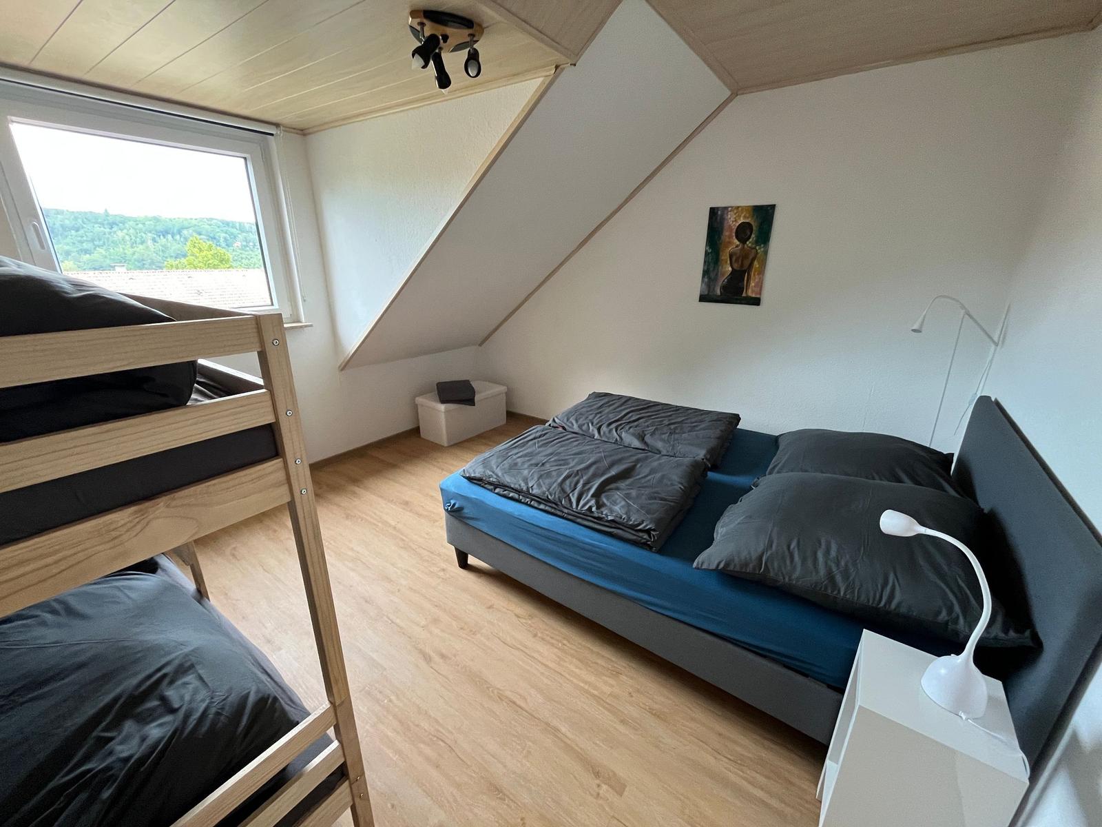 Schlafzimmer mit Doppelbett, Etagenbett und Fenster mit Blick auf Landschaft.
