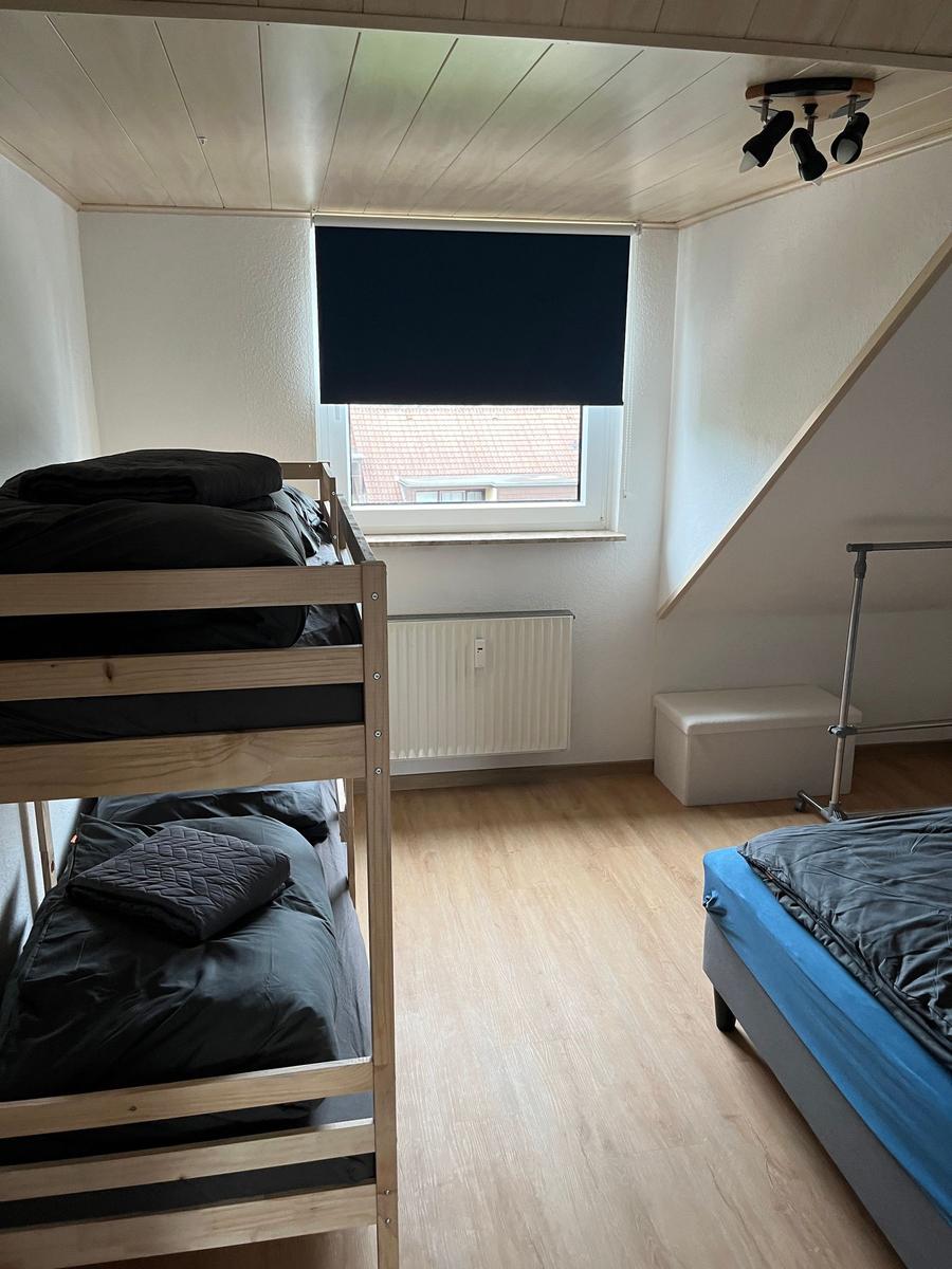 Zimmer mit Doppelstockbett, Einzelbett, Fenster und Heizung.