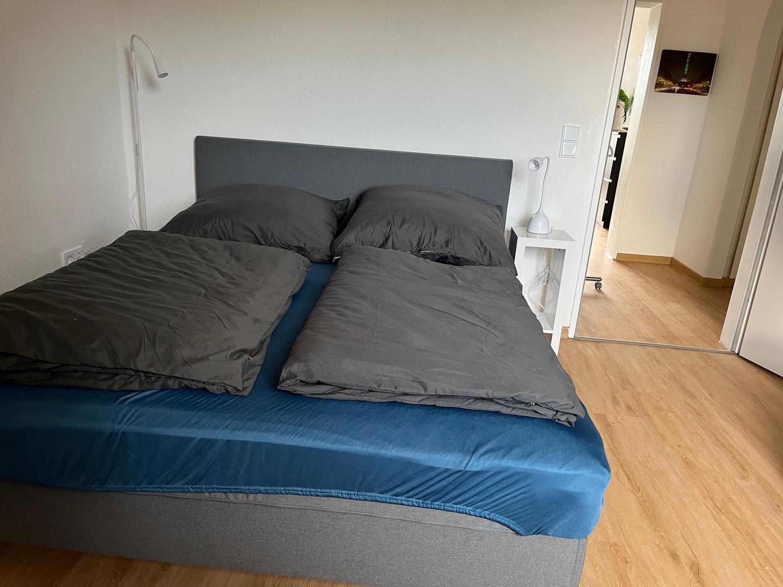 Doppelbett mit grauer Bettwäsche und blauer Matratzenhülle.