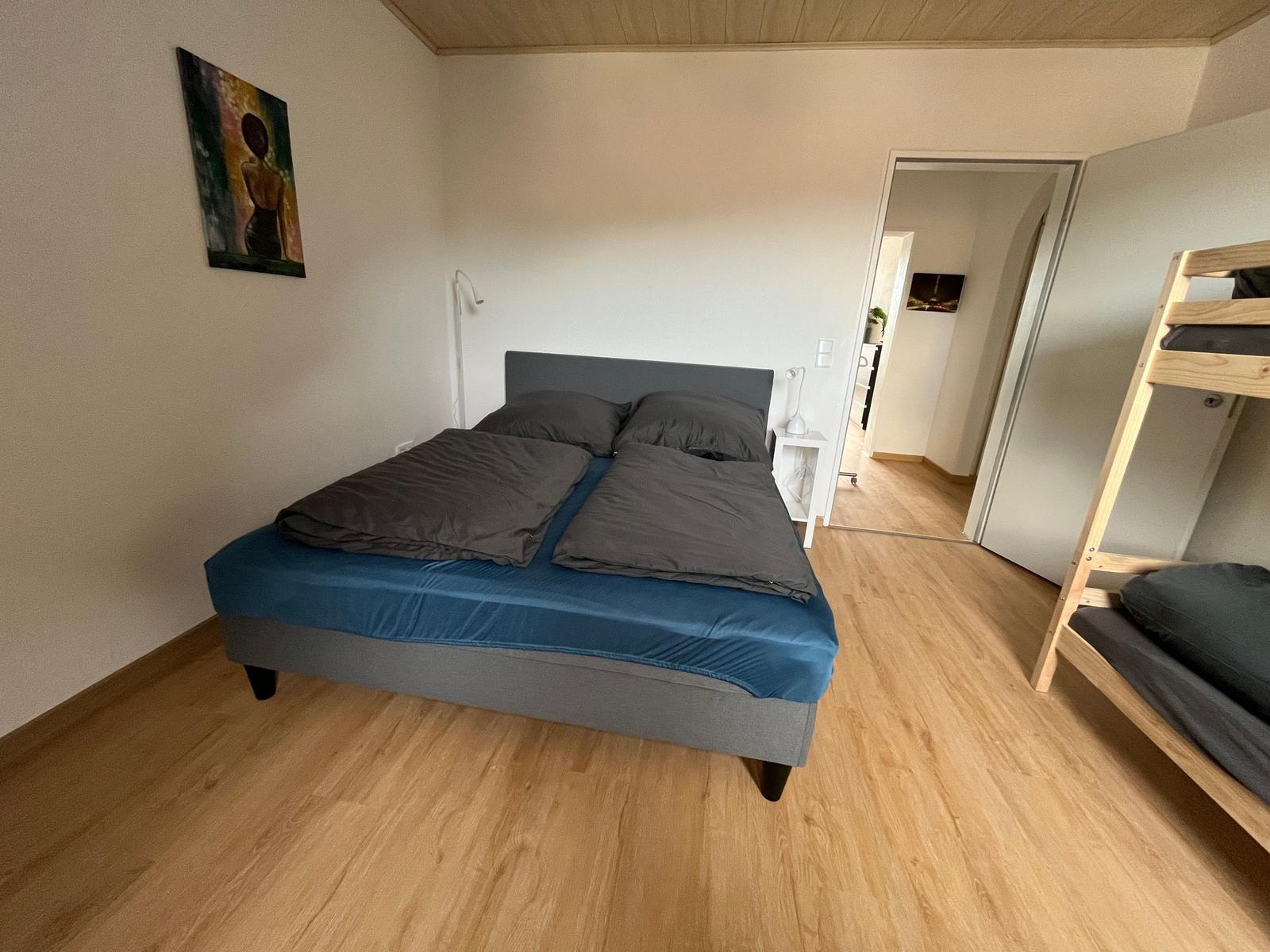 Schlafzimmer mit Doppelbett und Kletterbett. Holzboden und Wandbild.
