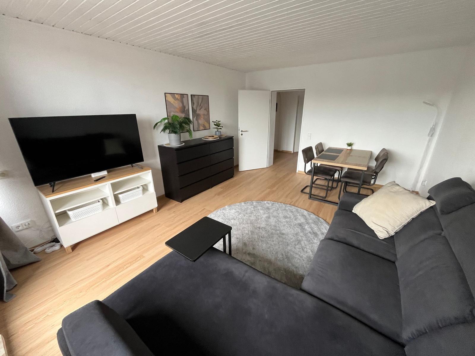 Wohn- und Essbereich mit Sofa, Fernseher und Esstisch.