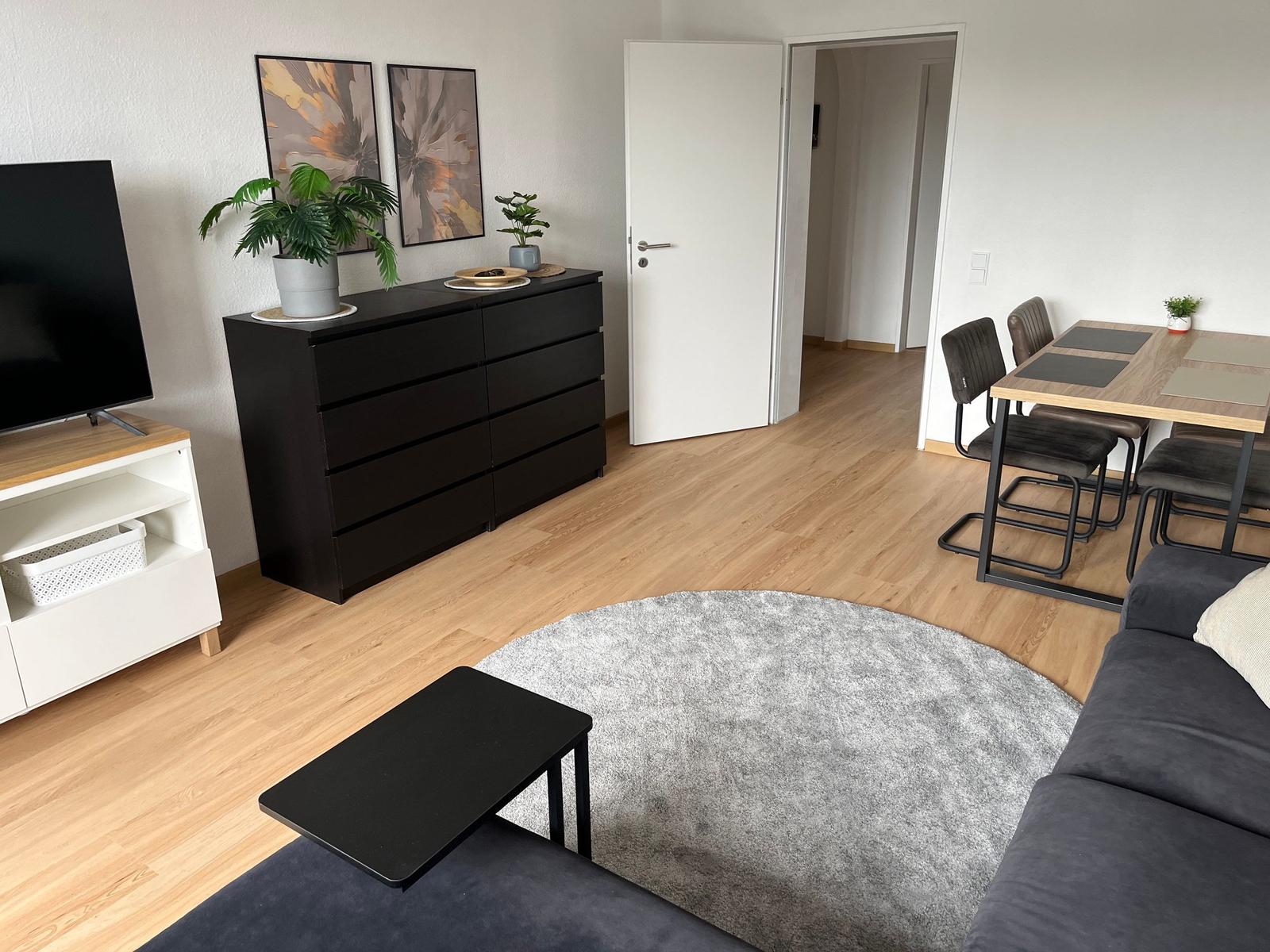 Wohnzimmer mit Sofa, Esstisch und Schrank. Holzboden und grauer Teppich.
