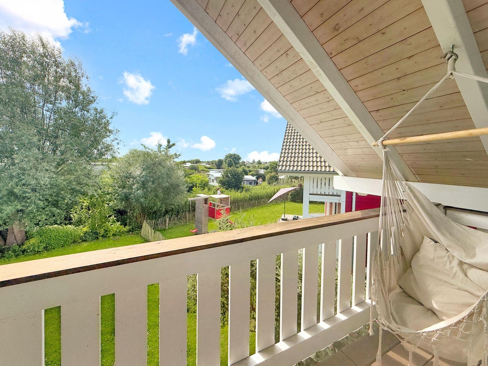 Terrasse mit Hängematte und Blick auf grünen Garten und Haus.