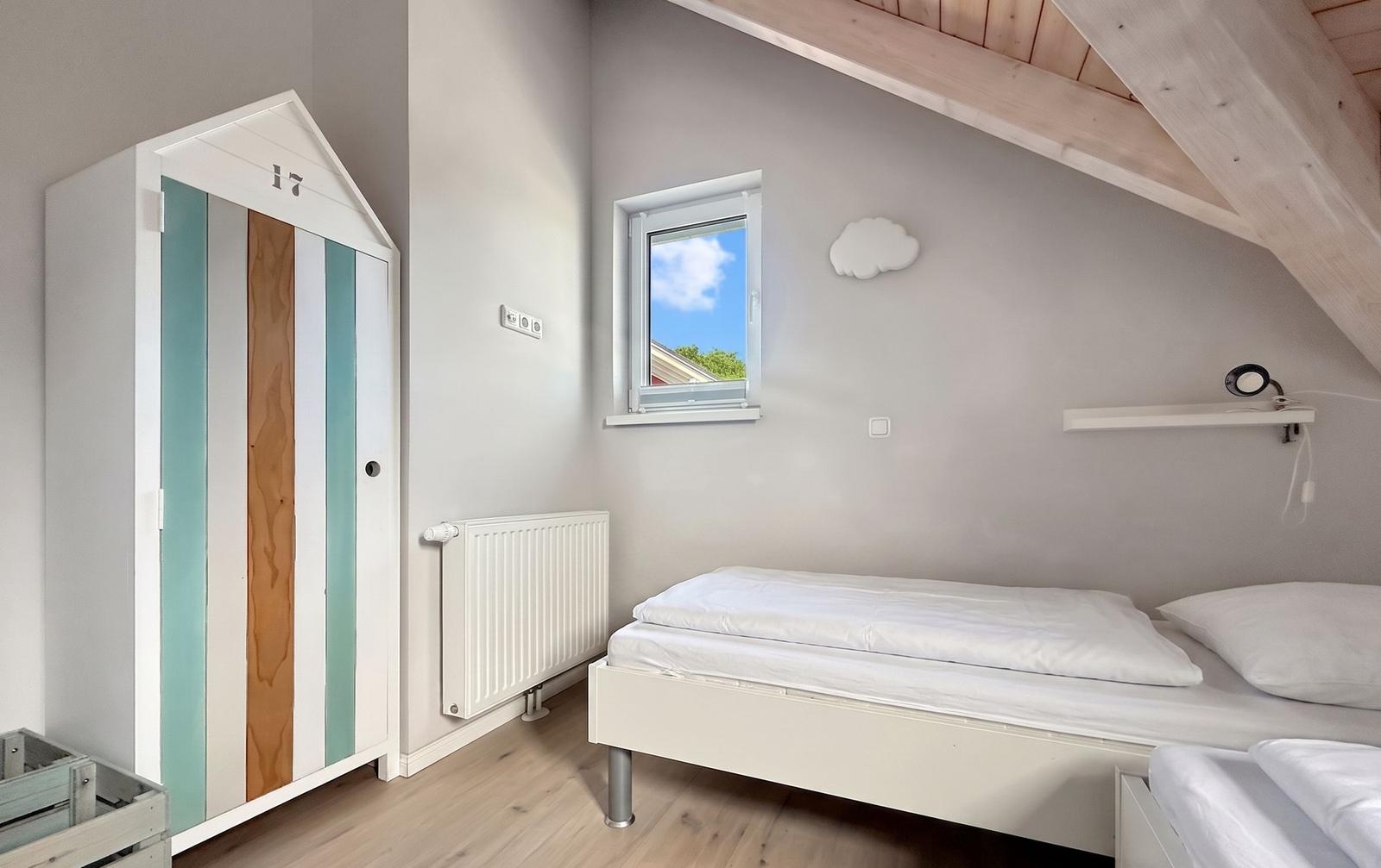Schlafzimmer mit Dachschräge, Bett, Kleiderschrank und Fenster mit Blick nach draußen.