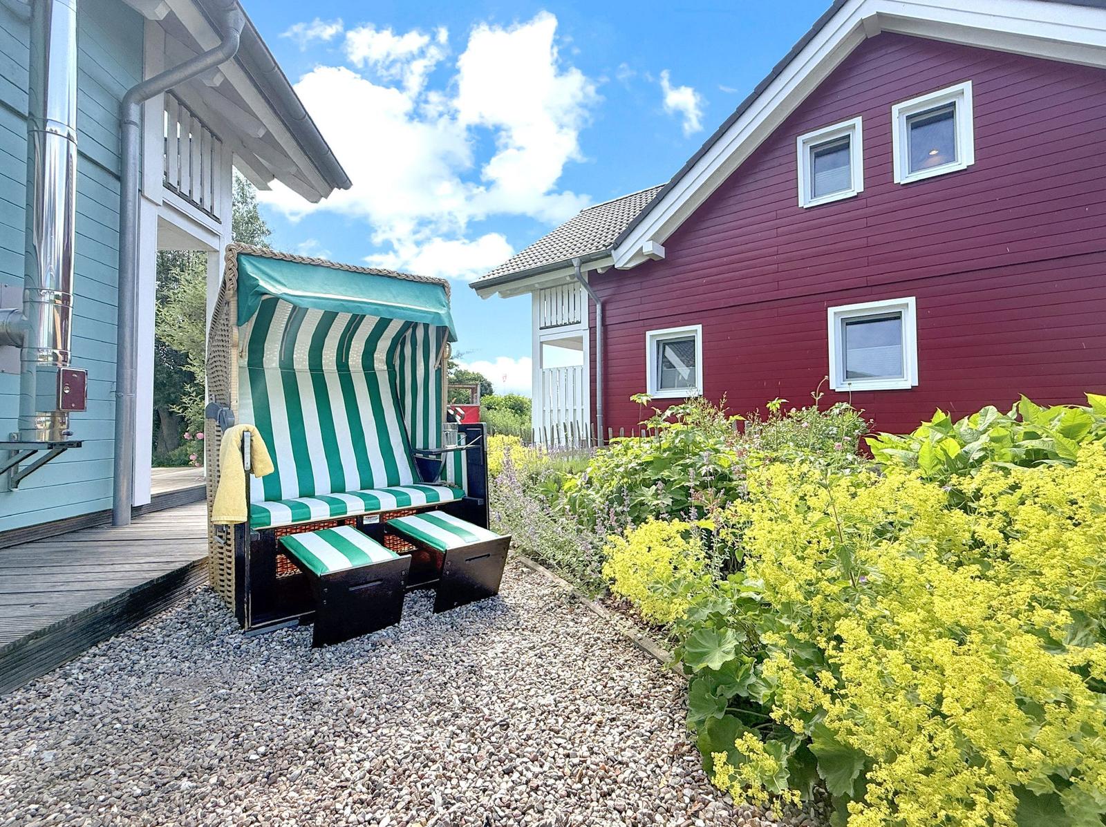 Grüner Strandkorb mit grün-weißem Streifenmuster steht auf Kies vor einem roten Haus.