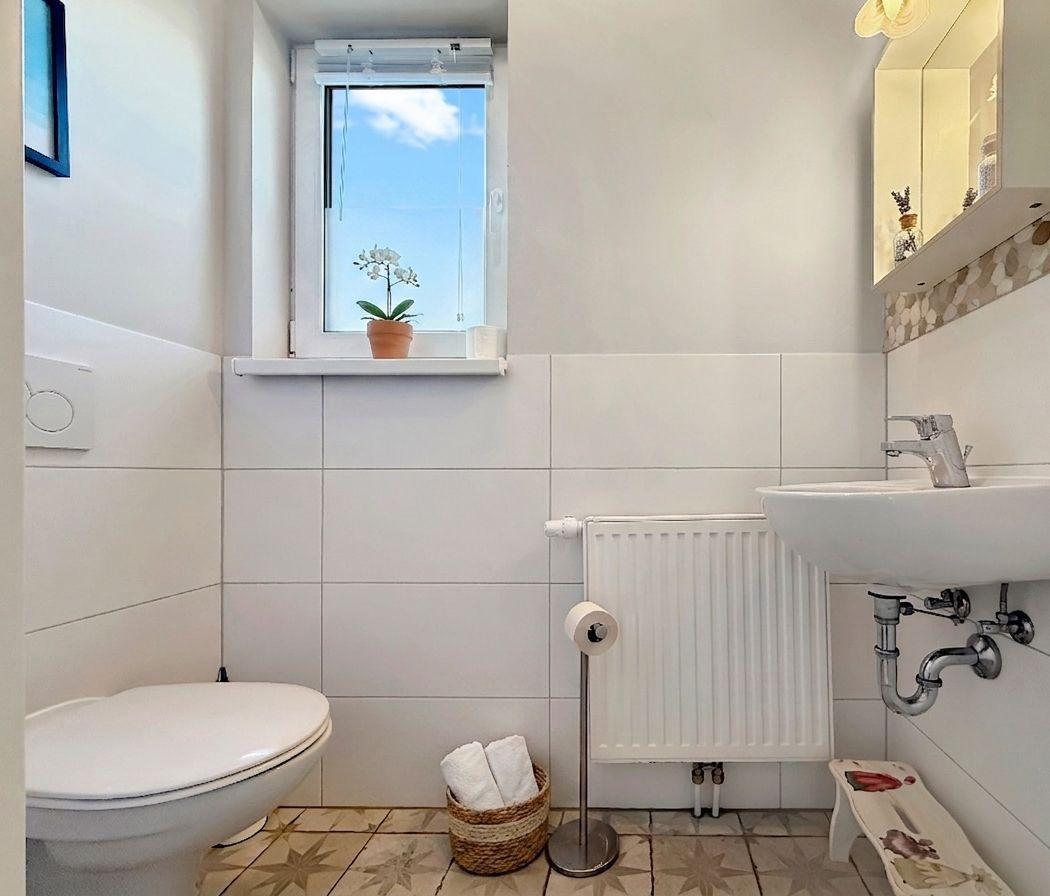 Badezimmer mit Toilette, Waschbecken und Fenster mit Pflanze.