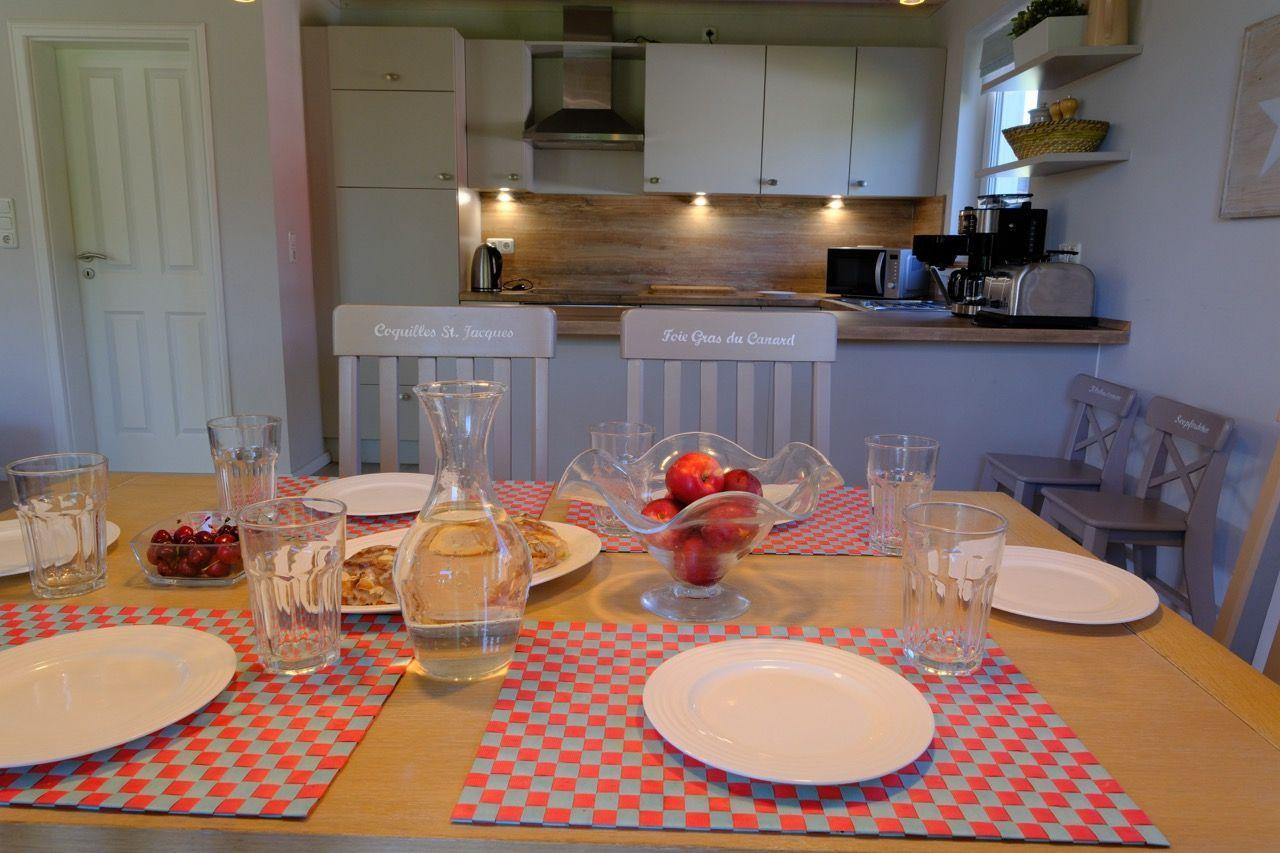 Esszimmer mit Tisch, Stühlen und Küchenbereich im Hintergrund.