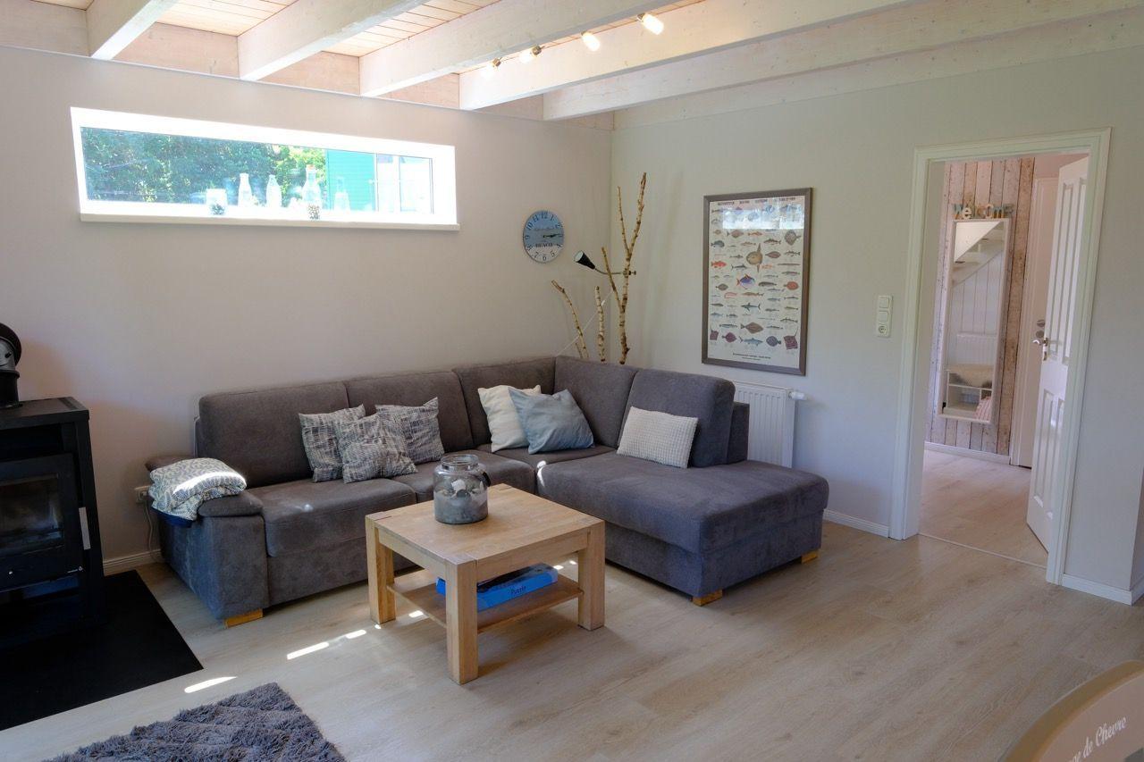 Wohnzimmer mit grauem Sofa, Holztisch und Fenster. Durchgang zu einem anderen Raum.