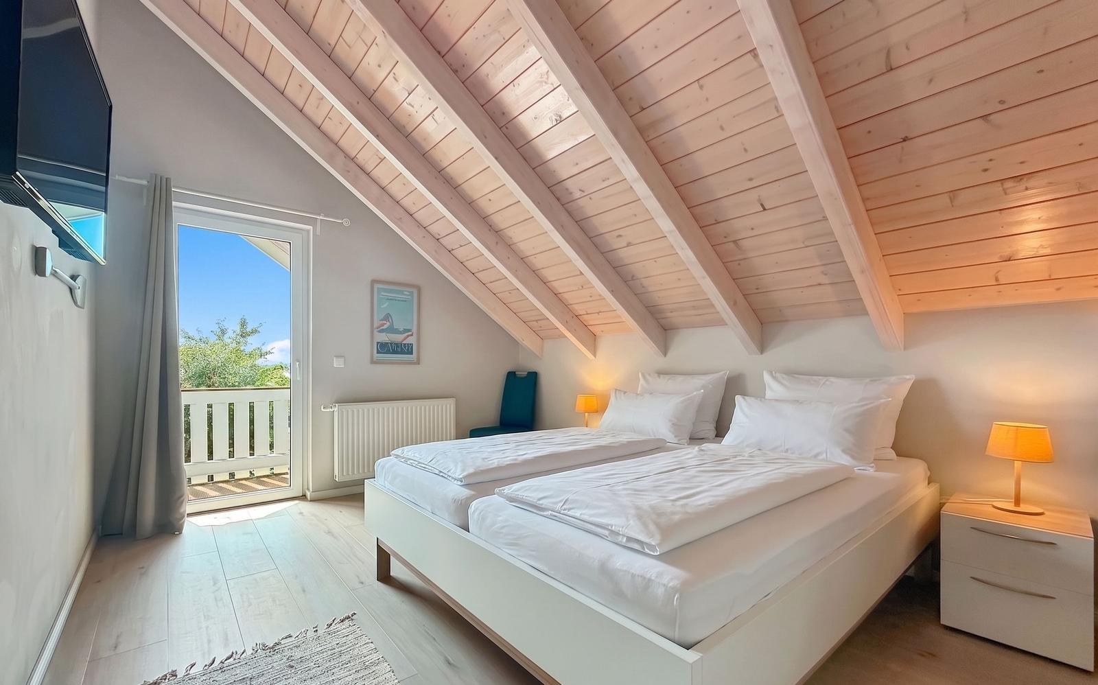 Schlafzimmer mit Doppelbett, Holzdecke und Balkontür. Fernseher und Nachttische vorhanden.