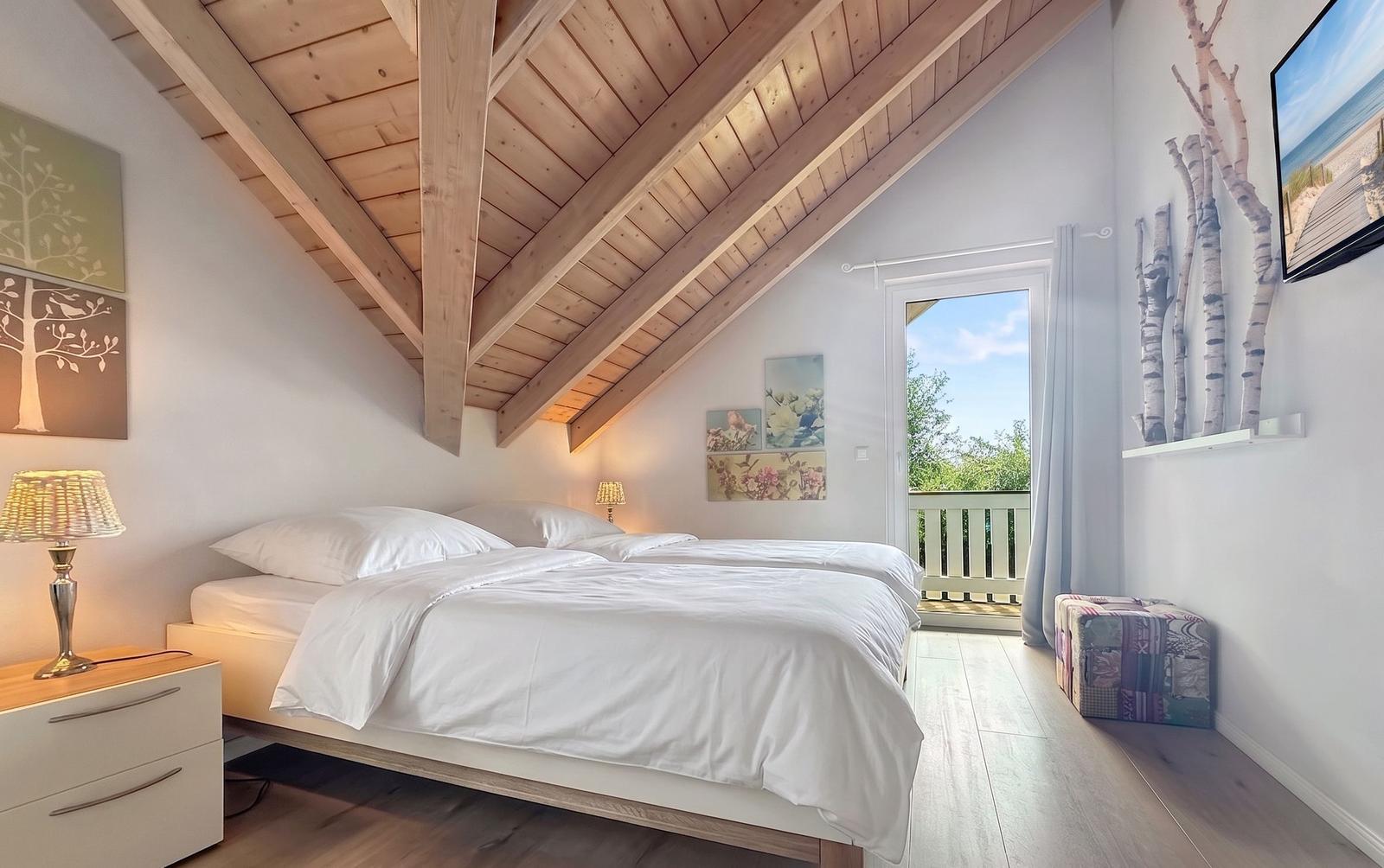 Schlafzimmer mit Dachschrägen, Bett, Nachttisch und Balkonzugang.