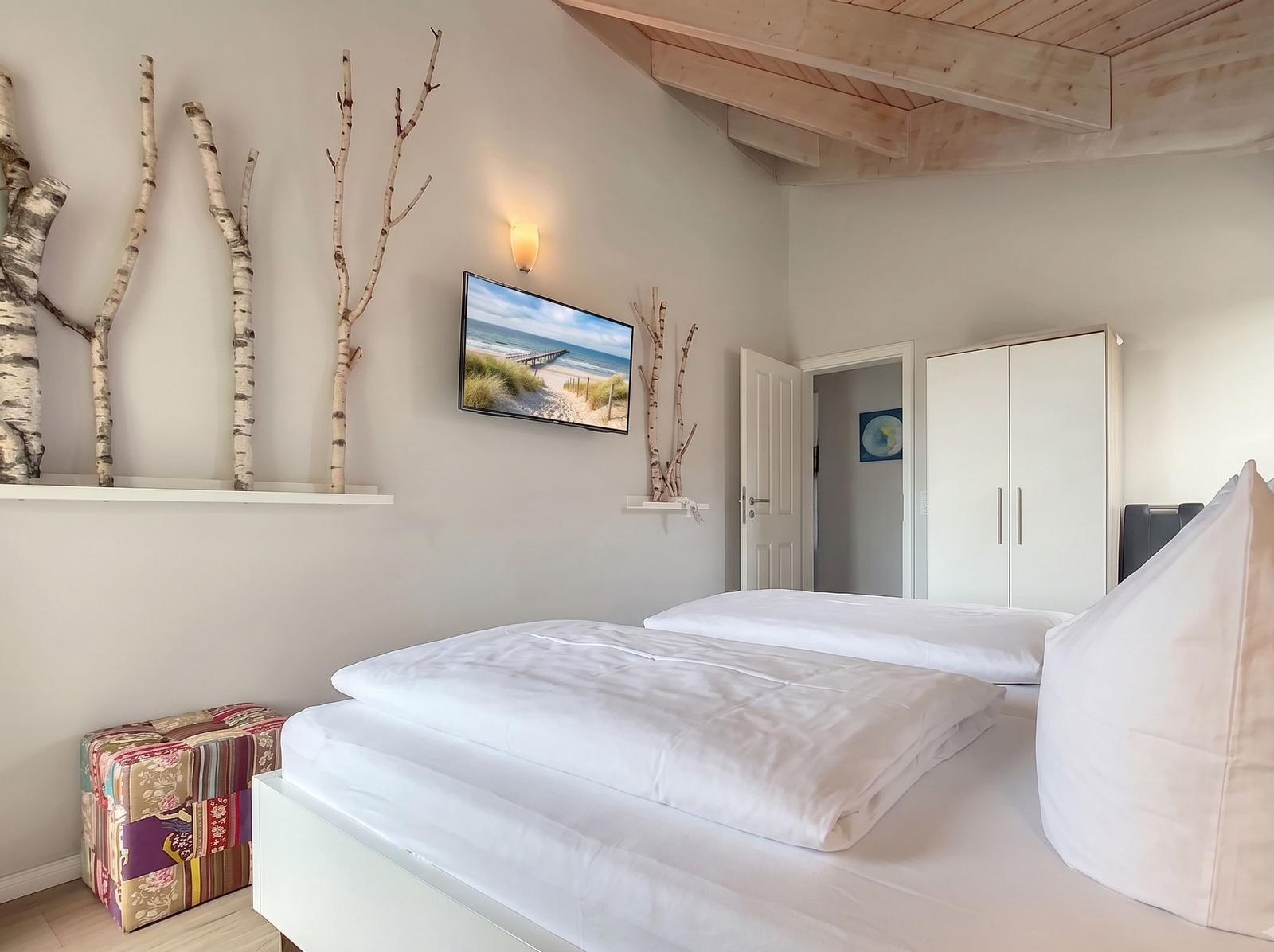 Schlafzimmer mit Doppelbett, Fernseher und Holzbalkendecke.