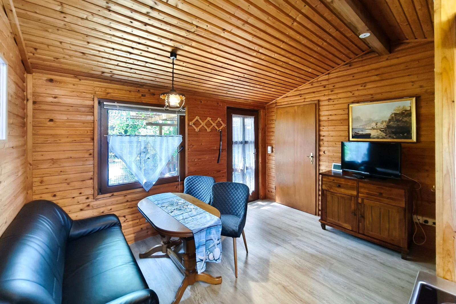 Wohnzimmer mit Holzwand, Sofa, Tisch, Stühle und Fernseher.