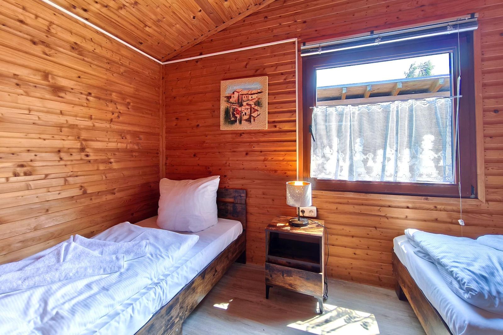 Zimmer mit zwei Betten, Holzwand und Fenster mit Vorhang.