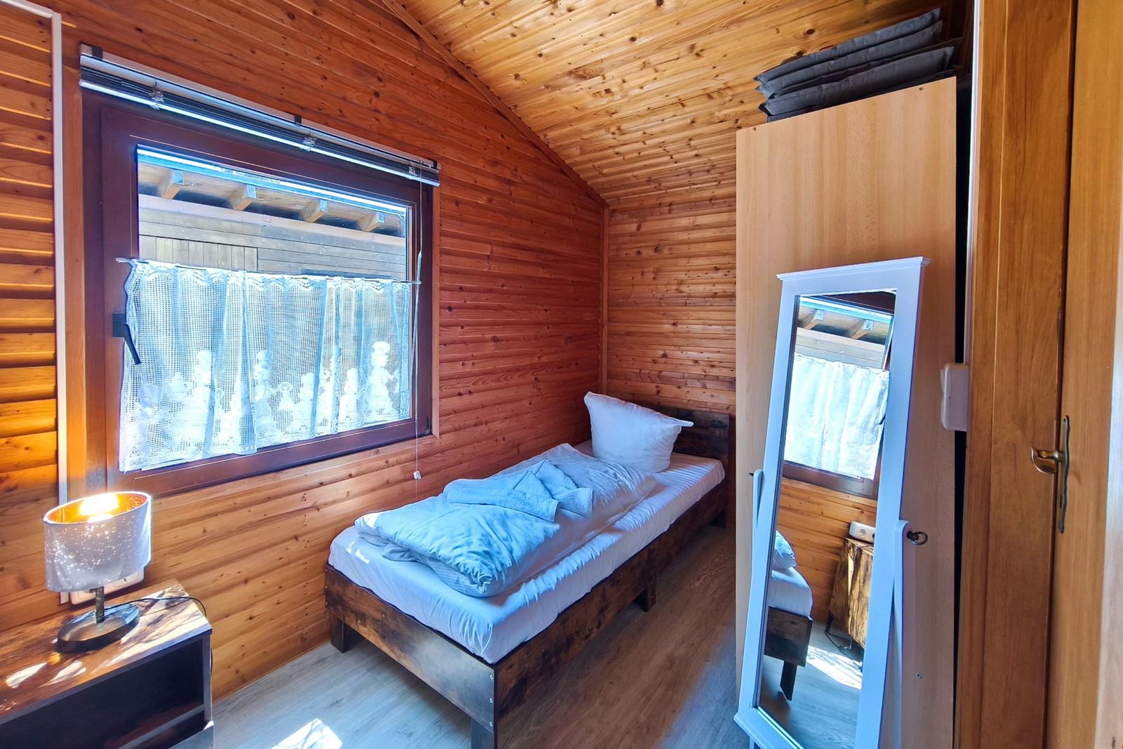 Ein Schlafzimmer mit Holzwand, Bett, Spiegel und Fenster mit Vorhang.