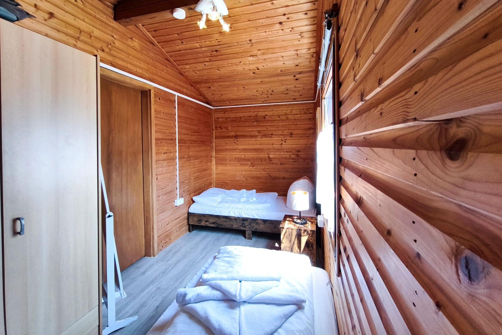 Zimmer mit Holzwand, zwei Betten und Nachttisch mit Lampe.