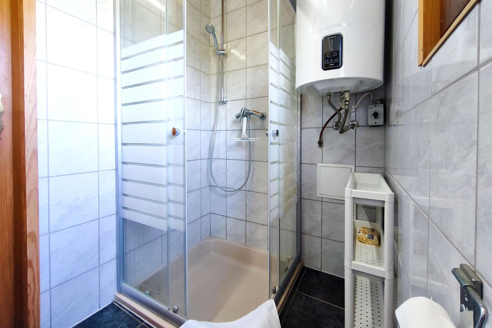 Duschkabine mit Glaswand, Heizung und Regal. Fliesenwand und Boden.