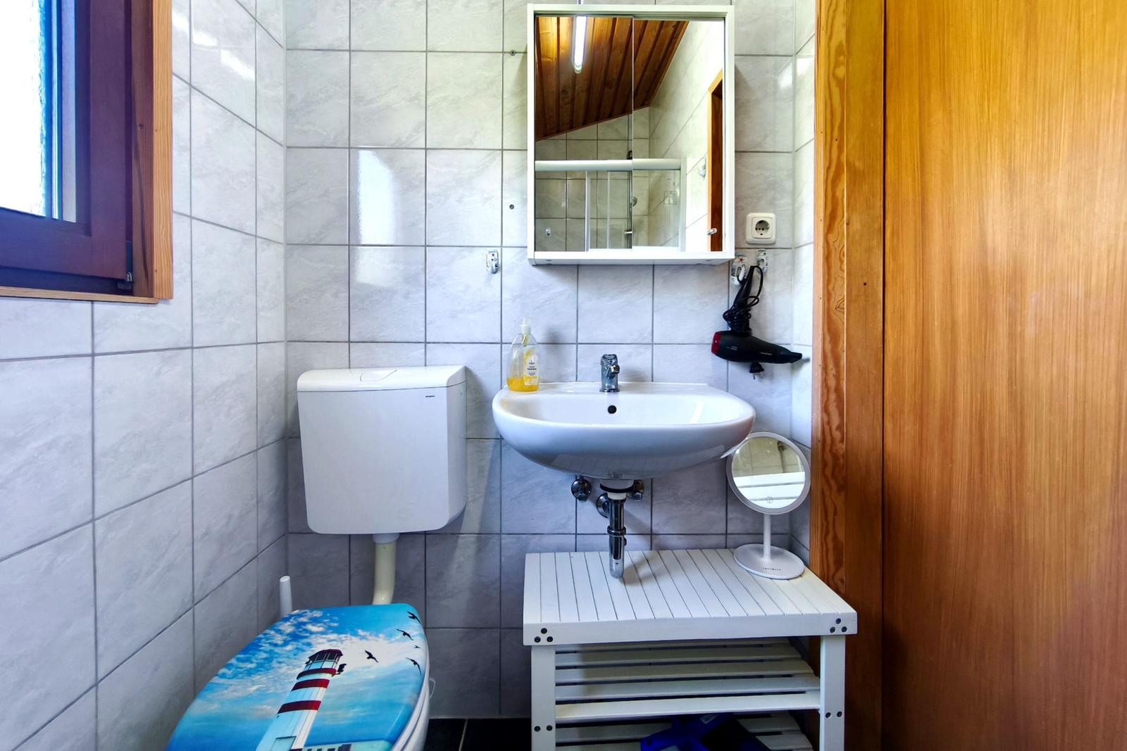 Badezimmer mit Waschbecken, Spiegel, Toilette und Fenster.