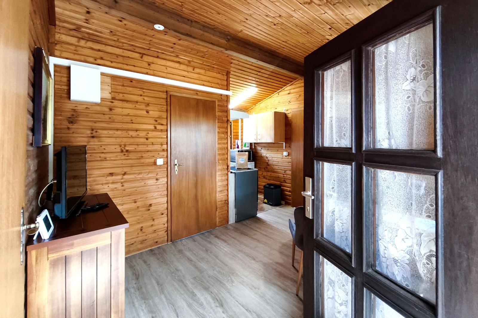 Wohnraum mit Holzwand, Fernseher und Tür zum Flur. Durchgang zu Küche und Wohnbereich.