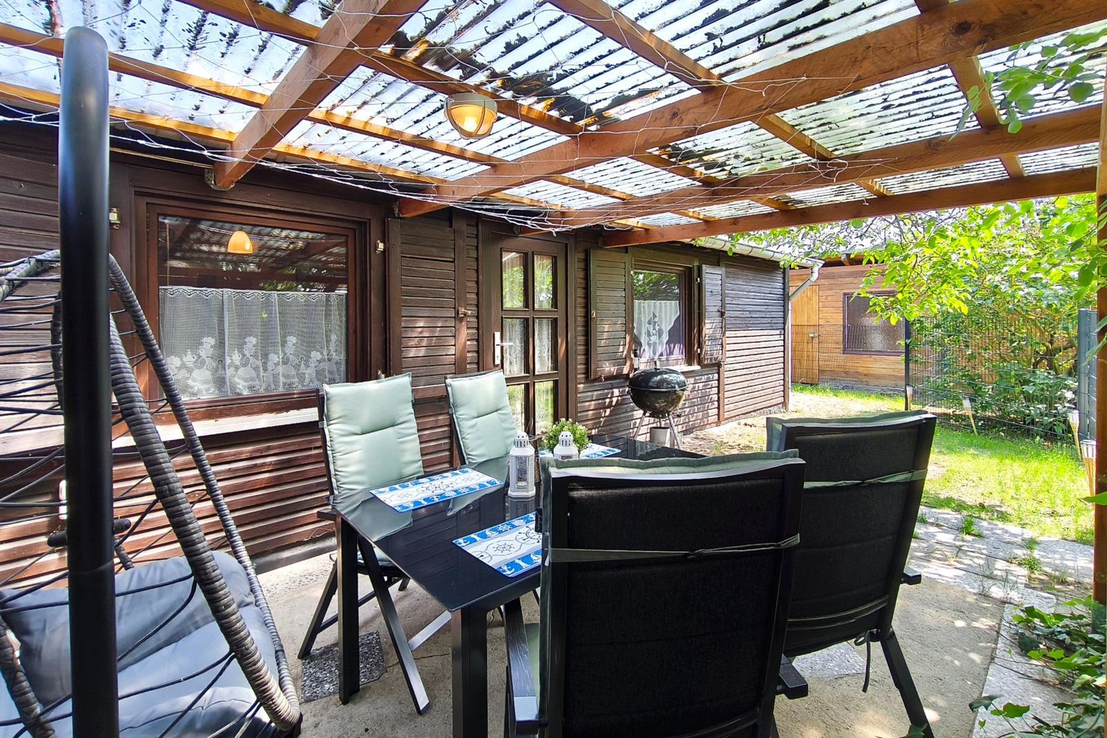 Terrasse mit Sitzgruppe, Grill und Holzüberdachung. Hinterhof mit Grünflächen.