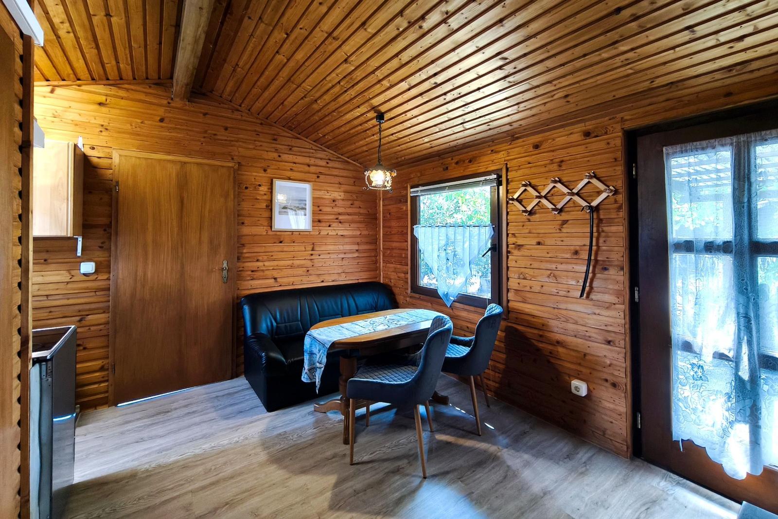 Wohnraum mit Holzwand, Tisch, Sofa und Fenster mit Gardine.
