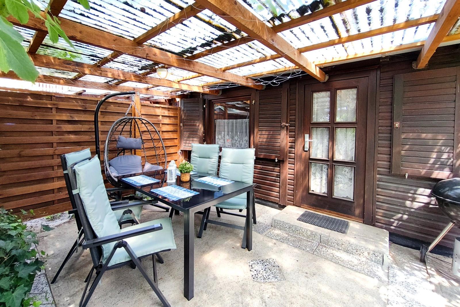 Terrasse mit Tisch, Stühlen und Hängesessel unter Holzüberdachung.