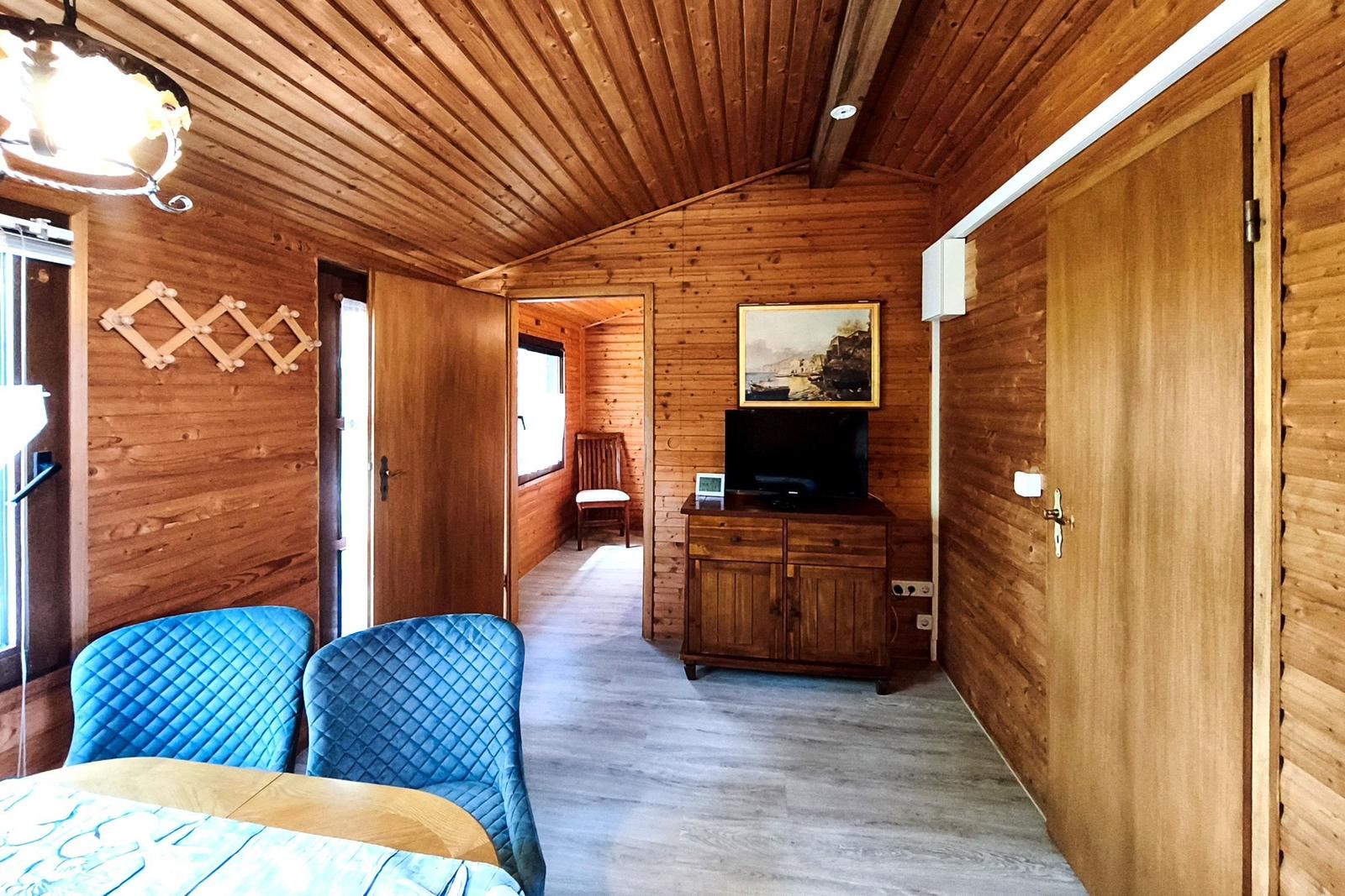 Wohnraum mit Holzwänden, blauen Stühlen und Fernseher auf Holzschrank.