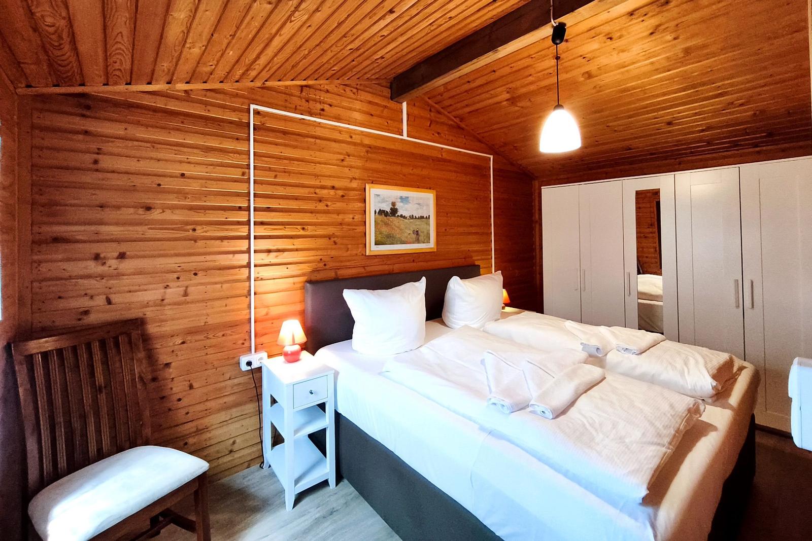 Schlafzimmer mit Holzwand, Bett, Nachttisch und Kleiderschrank.