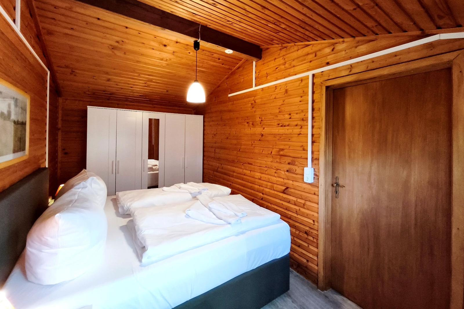 Schlafzimmer mit Holzwand, Bett, Kleiderschrank und Tür