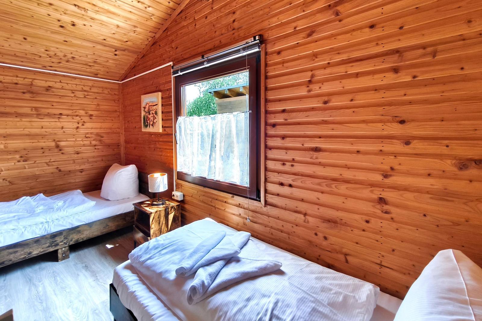 Zwei Betten in einem Holzhauszimmer mit Fenster und Nachttisch.