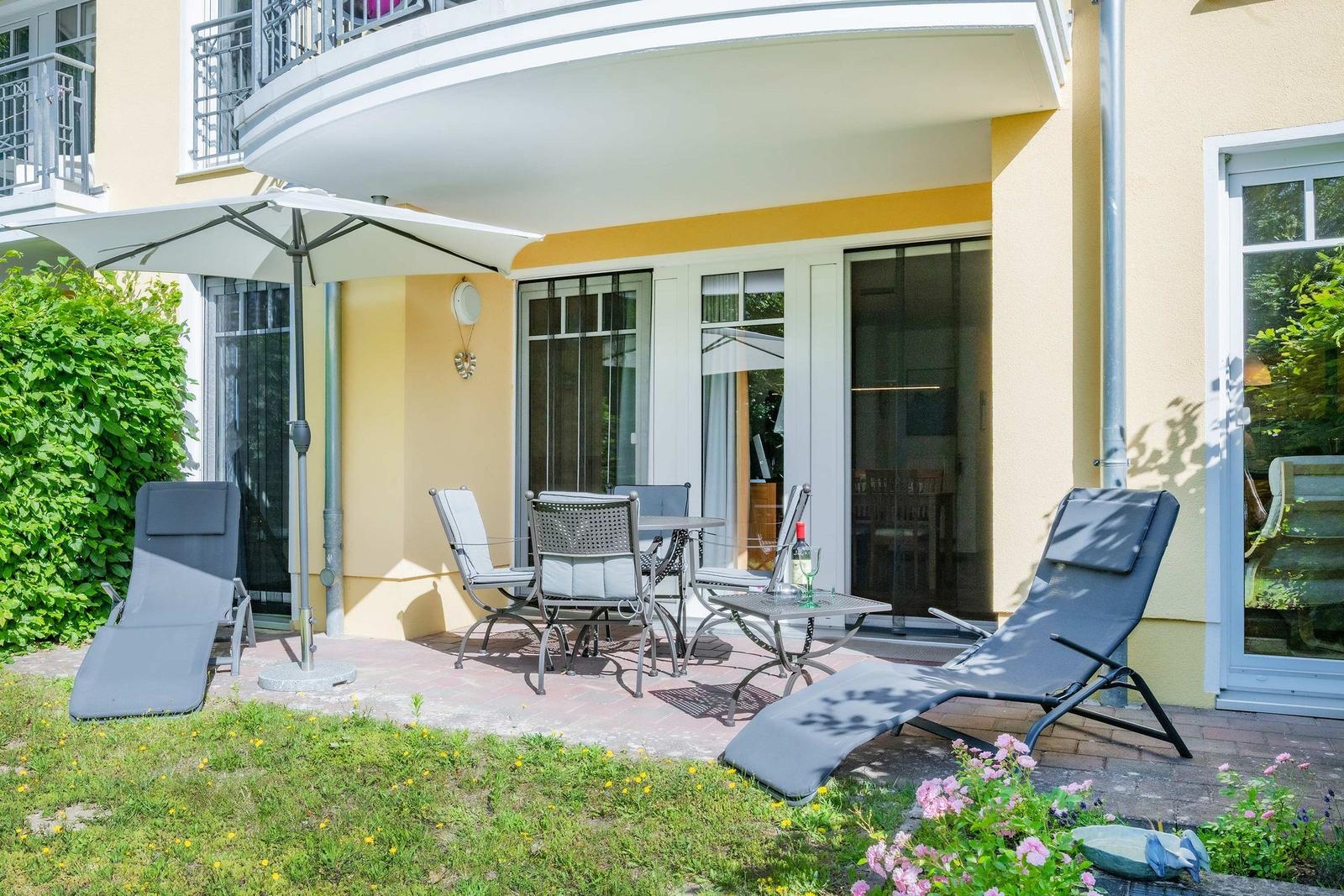 Terrasse mit Sitzgruppe, Sonnenschirm und Liegestühlen vor gelbem Haus.