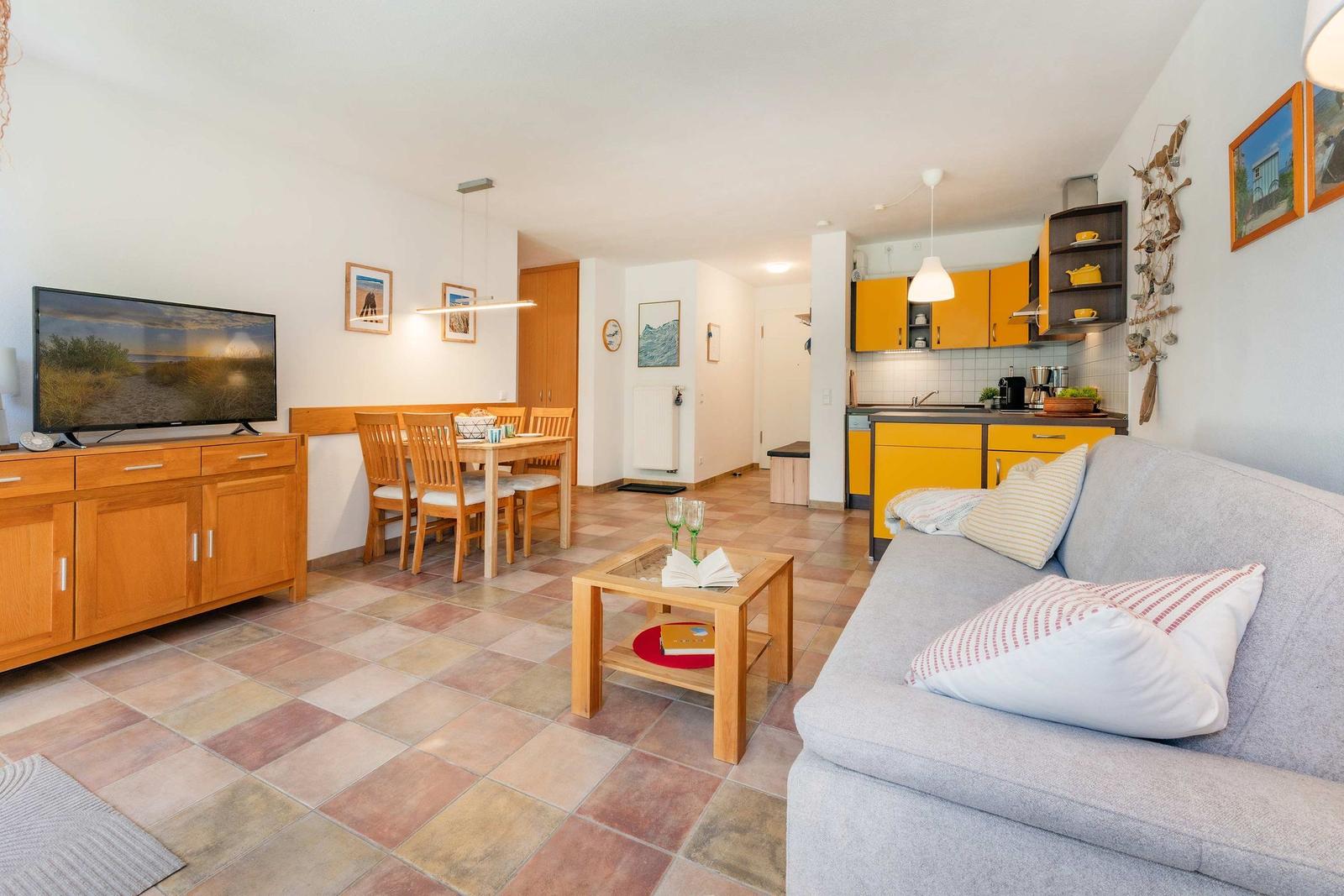 Wohnbereich mit Sofa, Essbereich und Küche mit gelben Schränken.