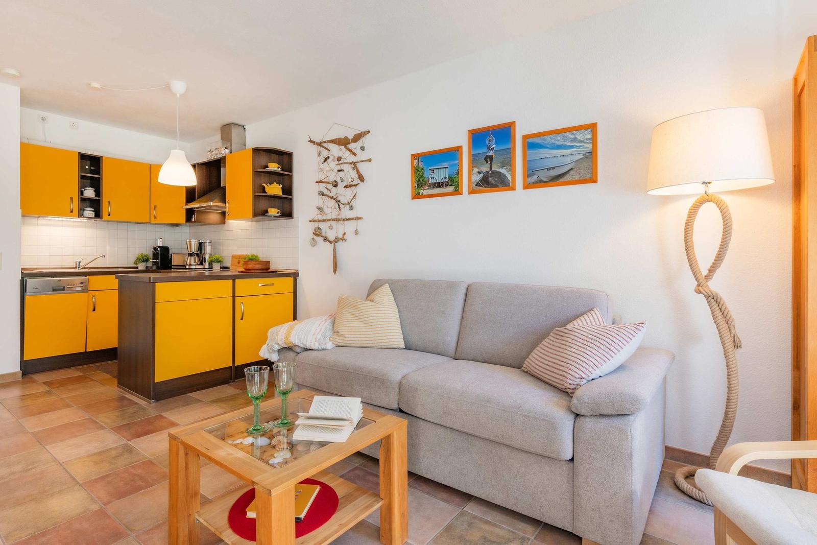 Wohn- und Küchenbereich mit grauem Sofa, gelben Schränken und Bodenfliesen.