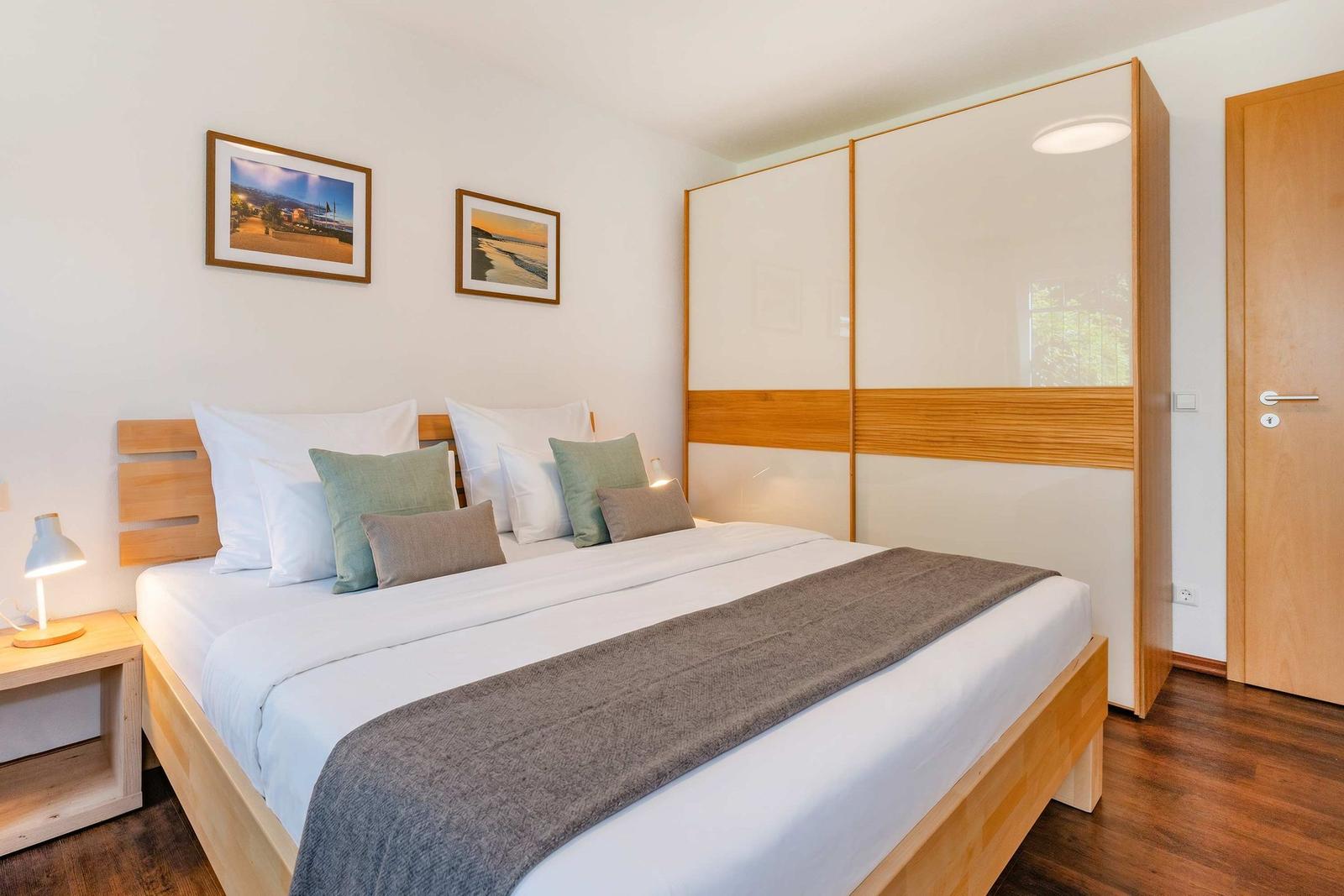 Schlafzimmer mit Doppelbett, Holzmöbel und Garderobe. Wandbilder und Nachttisch mit Lampe.