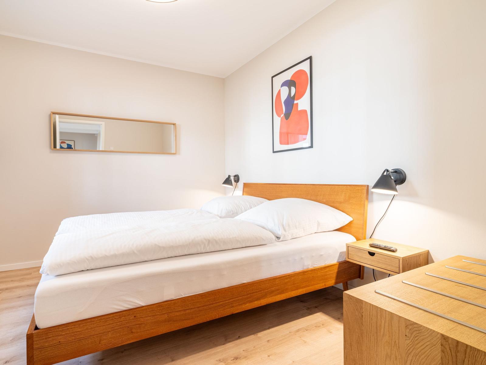Schlafzimmer mit Holzbett, Nachttisch und Wandbild.
