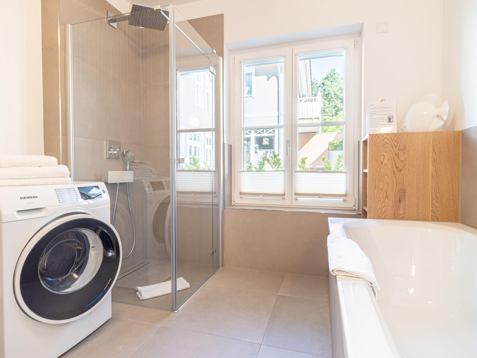 Badezimmer mit Dusche, Badewanne und Waschmaschine. Fenster mit Blick nach draußen.
