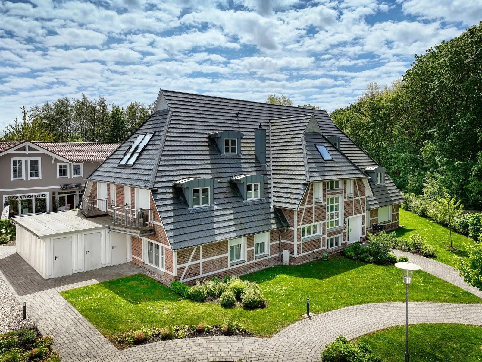 Haus mit grauem Dach, Ziegelfassade und gepflegtem Garten unter blauem Himmel.