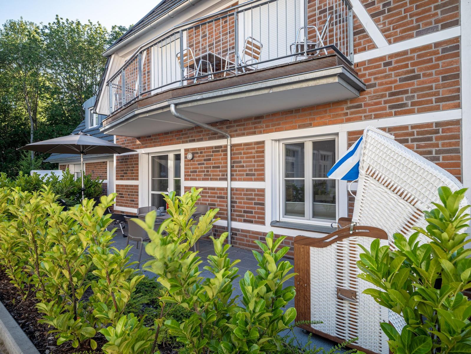 Terrasse mit Sitzgelegenheiten und Balkon an einem Backsteinhaus.